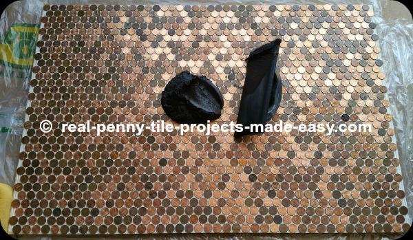 Black sanded grout about to be applied to pennies installed as tile on floor.