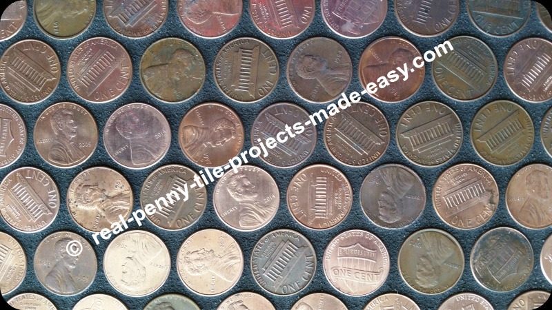 Close-up on dry grout the next day after black sanded grout was applied over tile sheets of real pennies. Notice how pennies are randomly placed and some pennies shine depending on angle of light.