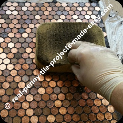 Using damp sponge to clean grout from floor of pennies.
