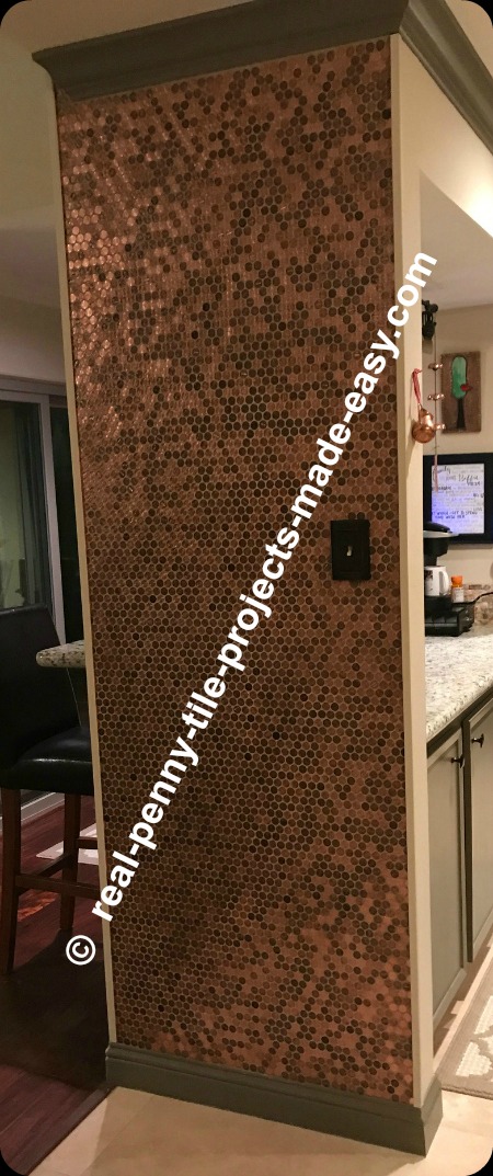 Pennies as mosaic tile sheets installed on a kitchen wall from floor to ceiling.