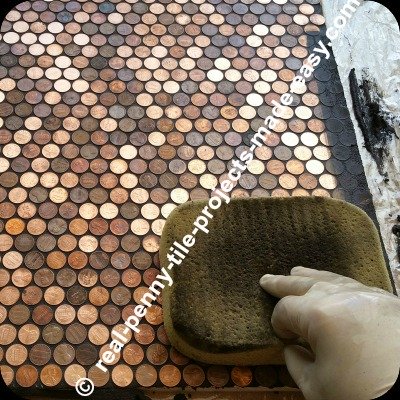 Washing/cleaning the black sanded grout from the surface of pennies. Cleaning started almost immediately after spreading the grout, to avoid grout drying hard on pennies.