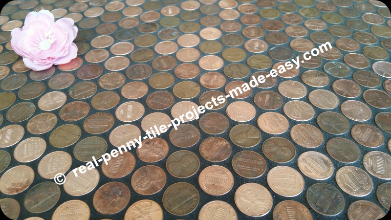 Flower sitting on top of floor covered in pennies grouted black.