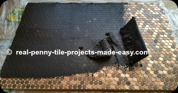 Grout application over tile sheets of real pennies. We chose SANDED black grout. The grout float is used to gently spread and push grout down in between and even under the edges of pennies.